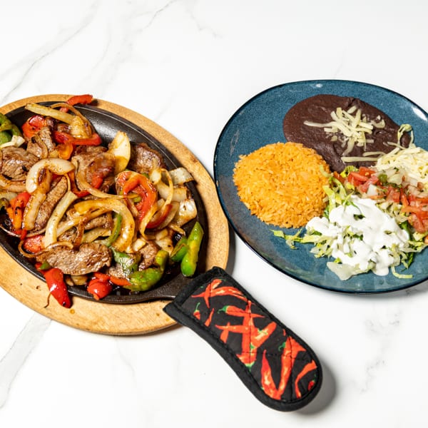Sizzling steak fajitas with onions and peppers, served with rice, black beans, and salad.