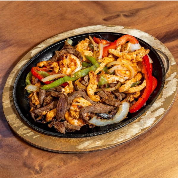 Sizzling fajitas with beef, chicken, shrimp, peppers, and onions in a cast iron skillet.