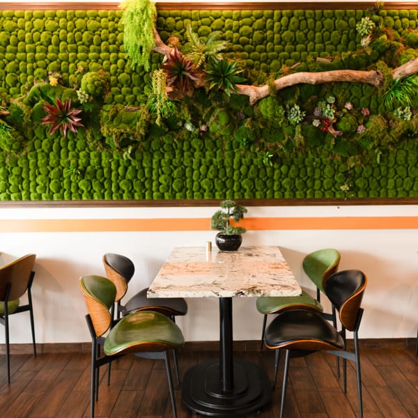 Restaurant interior featuring a vibrant green moss wall, marble table, and modern chairs.