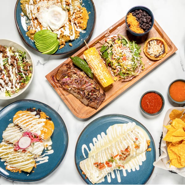 Overhead view of a spread of Mexican dishes, including enchiladas, steak, salad, and chips.