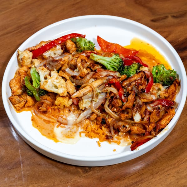Chicken, broccoli, cauliflower, onions, and red peppers with sauce and rice on a white plate.