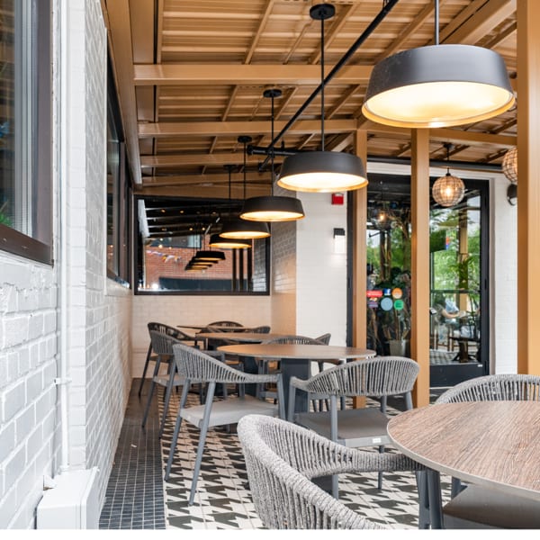Modern outdoor restaurant patio with grey woven chairs, round tables, and black and white patterned floor.