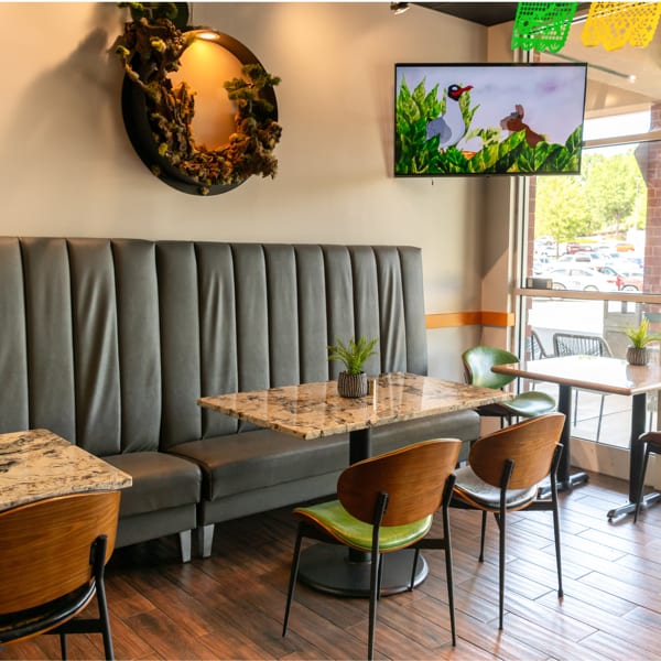 Restaurant interior with dark booths, marble tables, wooden chairs, a TV, and unique circular wall art.