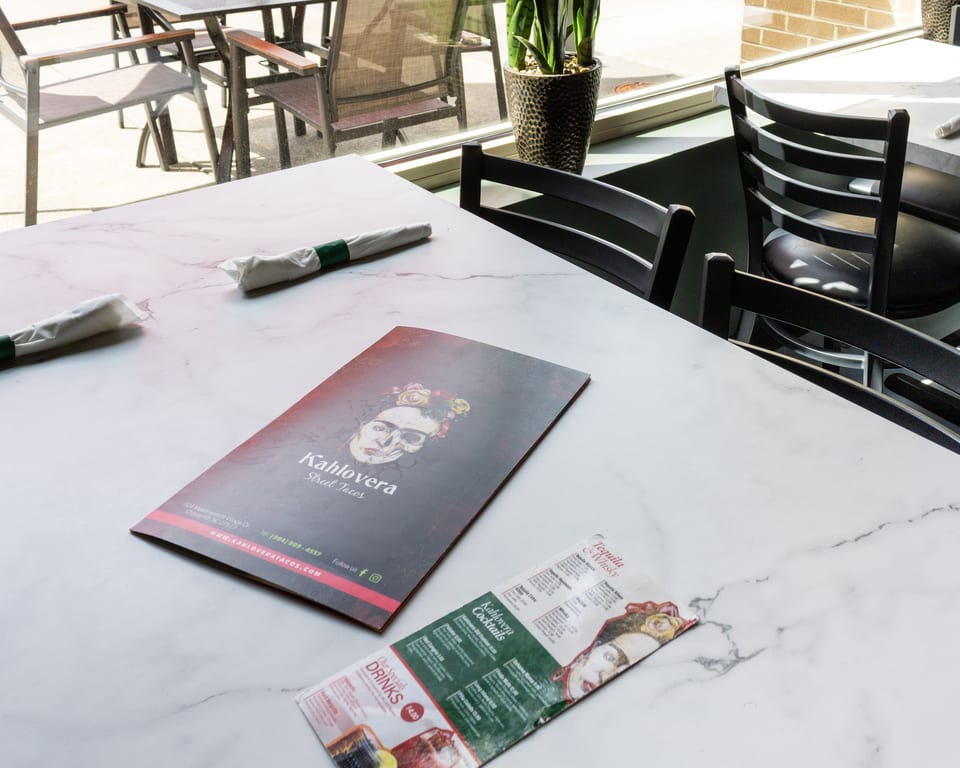 A Kahlovera Street Tacos menu and drink list on a white marble table with outdoor seating visible.