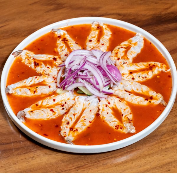 White plate of shrimp in a vibrant red sauce, topped with thinly sliced red onions.