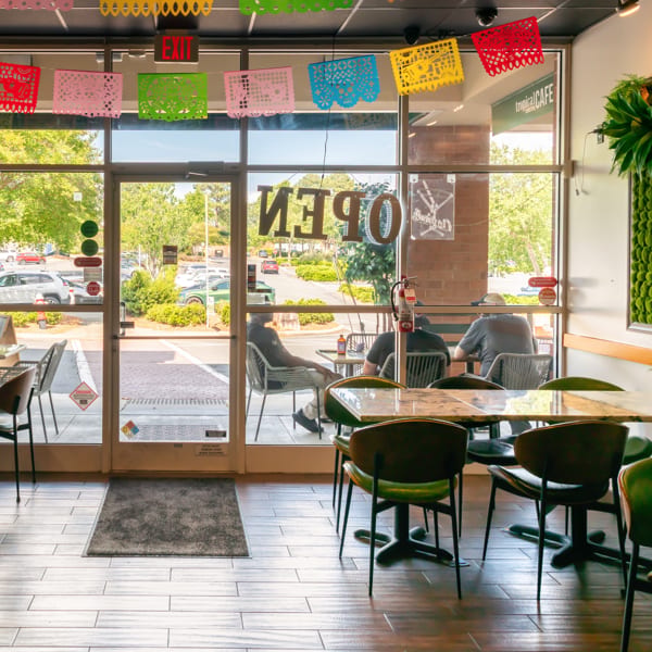 Bright Tropical Cafe interior with colorful papel picado, tables, and people seen through large windows.
