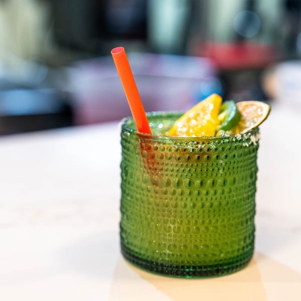 Green textured glass with a margarita, garnished with citrus slices, a jalapeño, and a red straw.