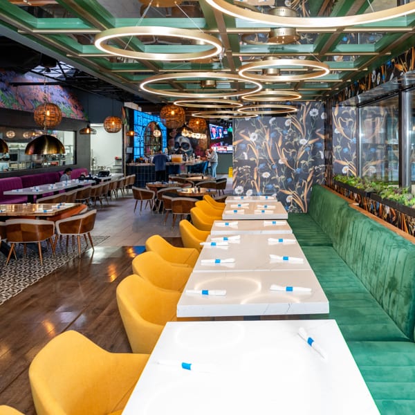 Vibrant restaurant interior with green booth, yellow chairs, white tables, and modern circular chandeliers.