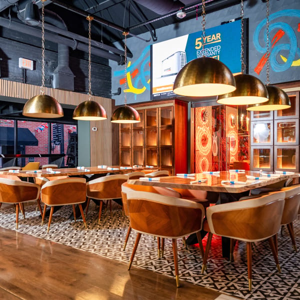 Elegant restaurant dining area with long wooden tables, modern chairs, brass pendant lights, and patterned floor.