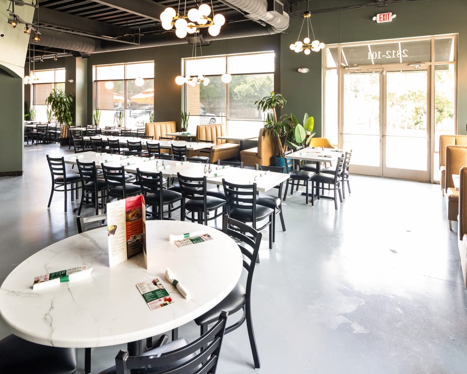 Spacious, modern restaurant interior with dark green walls, white marble tables, black chairs, and large windows.