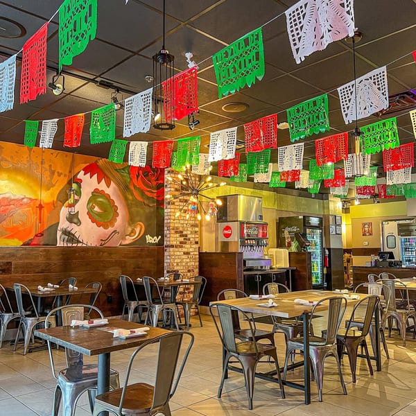 Vibrant Mexican restaurant interior with colorful papel picado, a large mural, and industrial-style tables and chairs.