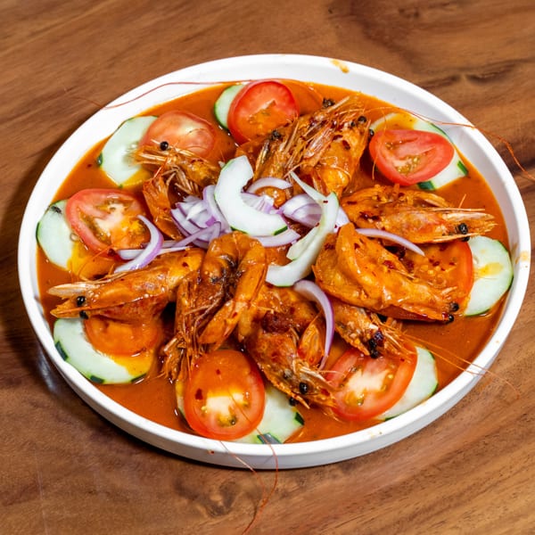 Whole prawns in a spicy red sauce, garnished with tomatoes, cucumbers, and red onions in a white bowl.