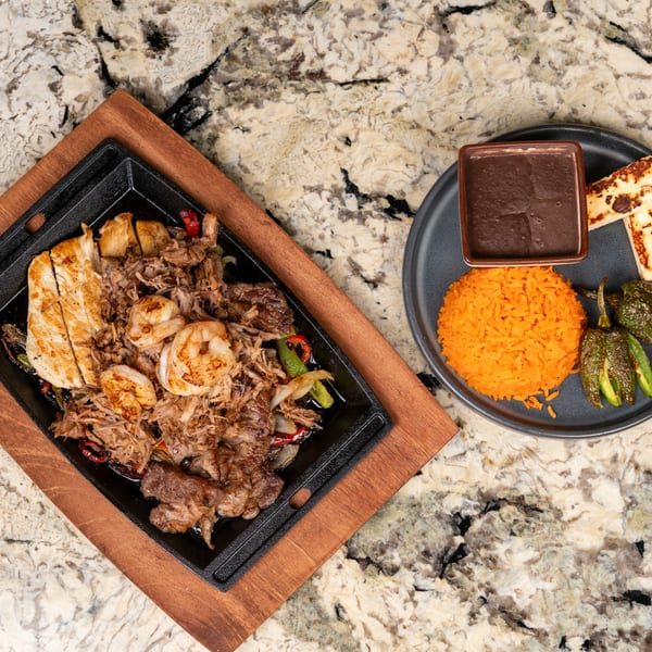 Sizzling fajita platter with chicken, shrimp, and beef, served with rice, beans, and grilled peppers.