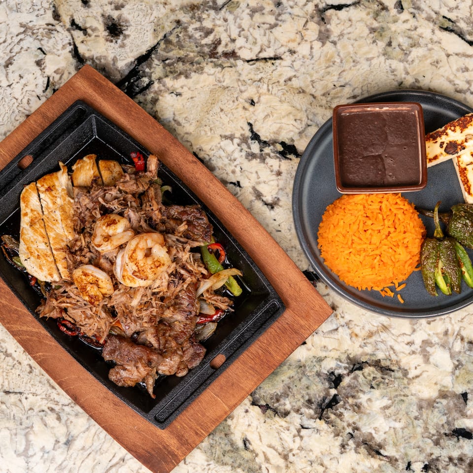Sizzling fajita platter with chicken, shrimp, and beef, served with rice, beans, and grilled peppers.