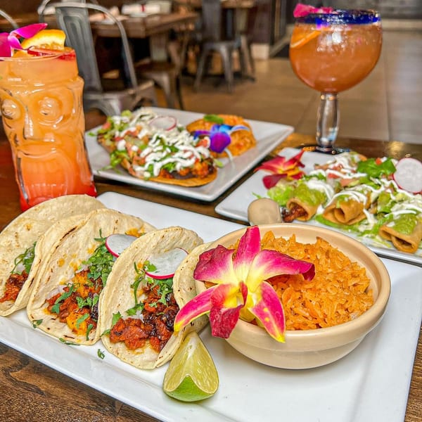 Tacos, rice, and other Mexican dishes with cocktails on a wooden table in a restaurant.