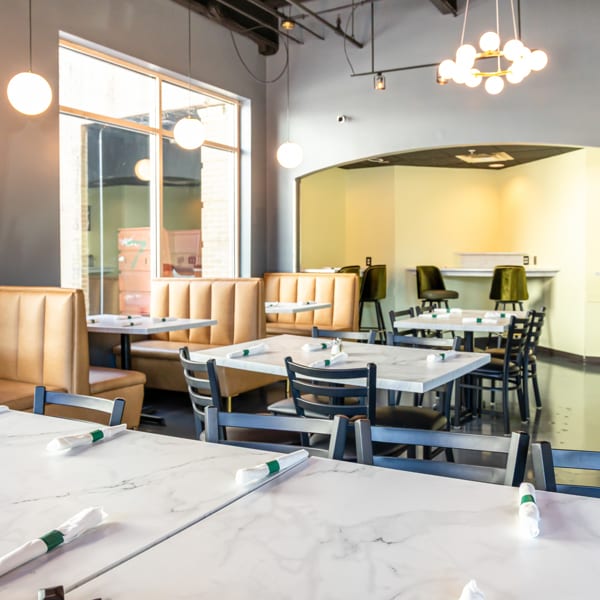 Modern restaurant interior with marble tables, dark chairs, tan booths, and contemporary lighting.