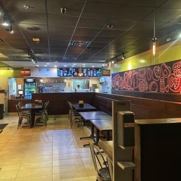 Casual restaurant dining area with wooden tables, metal chairs, and a vibrant food-themed wall mural.