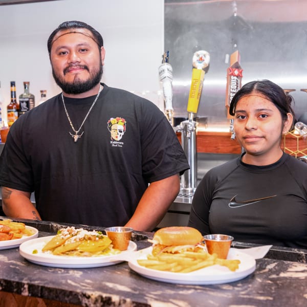 Kahlovera Street Tacos staff behind a counter with plates of tacos, a burger, and beer taps.
