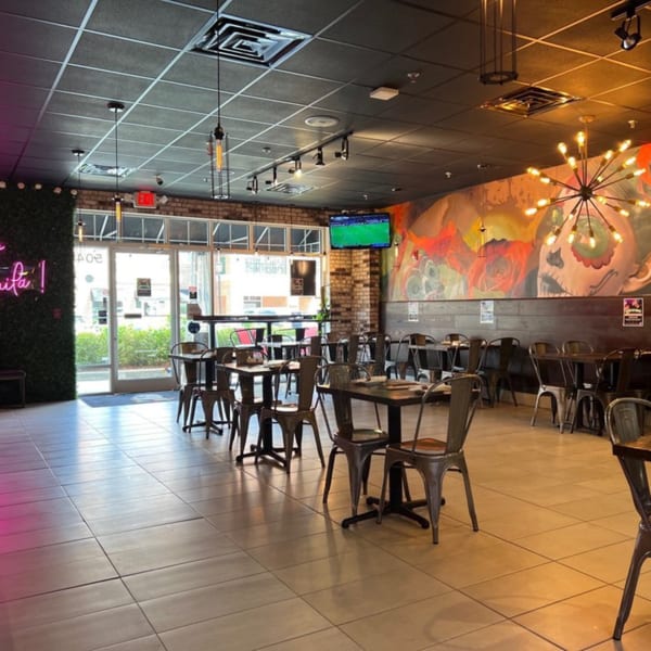 Empty restaurant dining room with industrial tables, chairs, a colorful mural, and modern lighting.