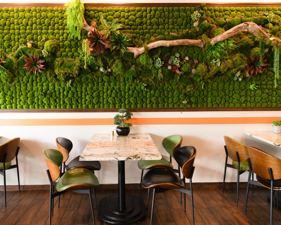 A restaurant dining area with a moss wall, marble tables, and modern green and black chairs.
