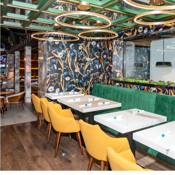 Modern restaurant interior with yellow chairs, green booth, floral wallpaper, and gold circular ceiling lights.