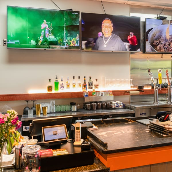A restaurant bar features three TVs, liquor bottles, beer taps, and a point-of-sale system.